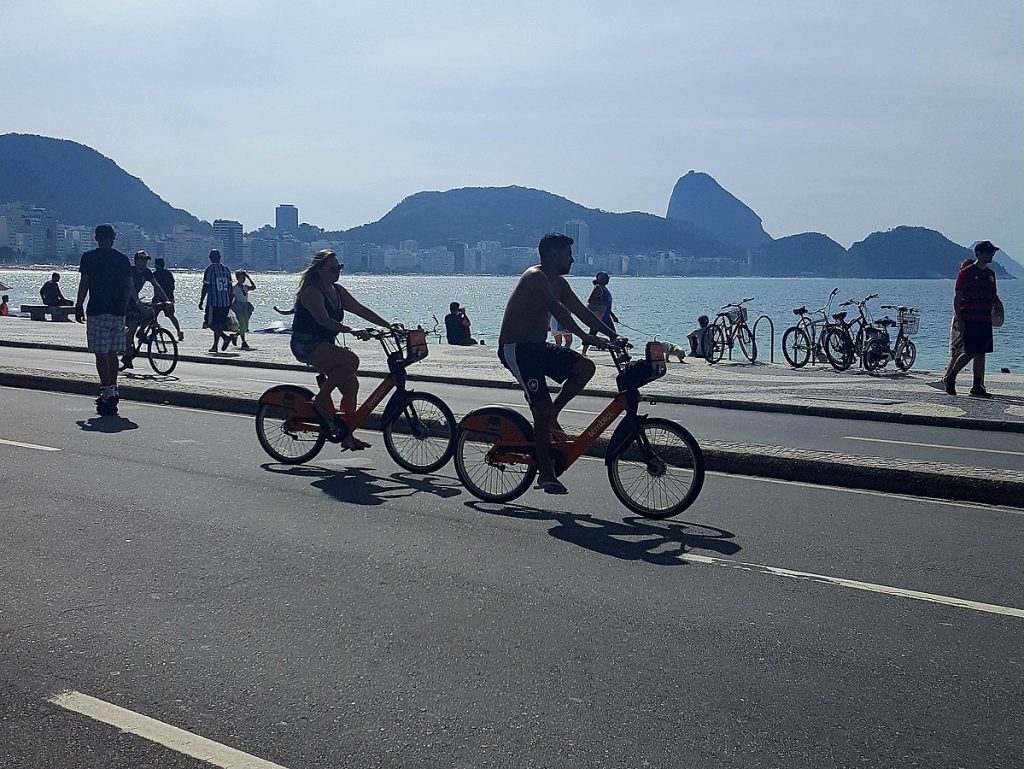 Dois usuários de bicicletas compartilhadas pedalam na rua ao longo da praia de Copacabana durante a ciclovia no Rio de Janeiro, Brasil. Data 12 de junho de 2018. Autor Dmy462
